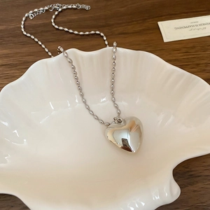 Minimalist silver heart pendant necklace with beaded chain on a white shell tray