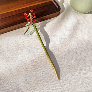 Close-up of handmade wooden hairpin with red beads and green leaf tassels