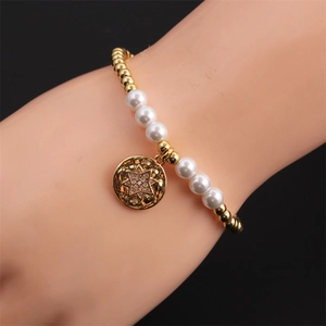Gros plan d'un bracelet de perles dorées avec pendentif étoile porté sur fond noir