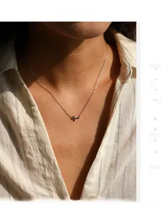 Detail of silver cross necklace with blue gems worn by a model in soft lighting