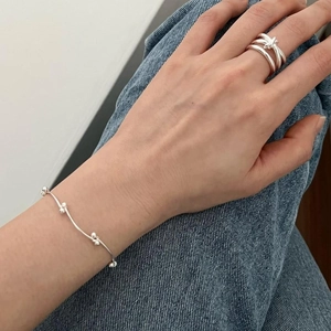 Close-up of minimalist S925 sterling silver beaded bracelet and layered knot ring on wrist