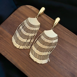 Detail of gold fan-shaped tassel drop earrings on a dark wooden display tray