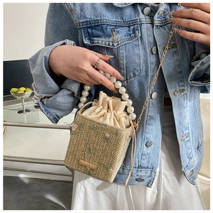 Detail of woven straw bucket bag with pearl handle and floral embroidery on a denim jacket