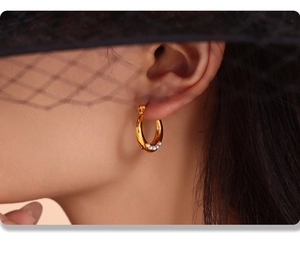Close-up of golden U-shaped titanium earrings with white pearls on a female model