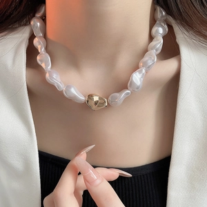 Détail d'un collier de perles baroques avec pendentif doré porté par un mannequin en blazer