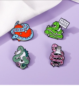 Close-up of four enamel snake brooches featuring heart, skull, and bottle designs