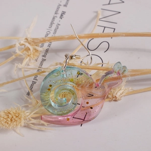 Detail of snail-shaped earring in blue-pink gradient acrylic with golden glitter inside