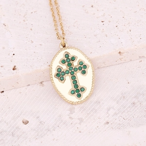 Detail of gold cross necklace with green gemstone inlay on textured stone background