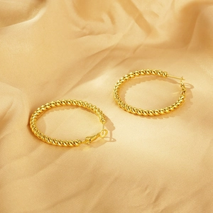 Macro shot of 18K gold plated twisted hoop earrings resting on champagne silk fabric