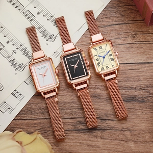 Close-up of three vintage square quartz watches with rose gold mesh bands on sheet music