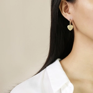 Close-up of a woman wearing gold heart earrings with a sparkling starburst center