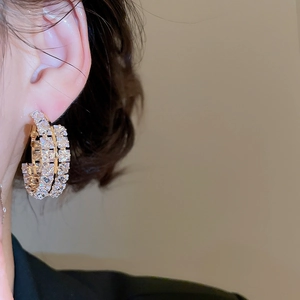 Détail de boucles d'oreilles créoles dorées en C serties de rangées de zircons carrés