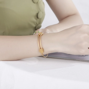 Detail of a gold double-layered heart charm bracelet worn by a model on a white surface