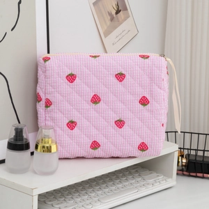Detail of pink quilted strawberry pouch with zipper closure on a white desk