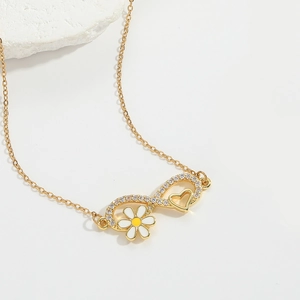 Macro detail of golden infinity necklace with daisy flower and heart zircon accents