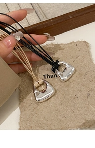 Dettaglio dei ciondoli a mini borsa in argento con cordini regolabili neri e beige