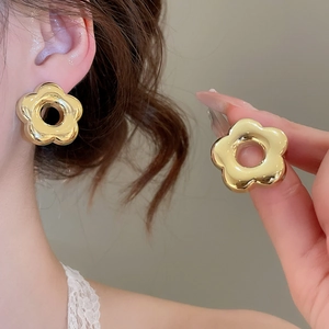 Vue détaillée de boucles d'oreilles fleurs dorées portées et tenues par un mannequin