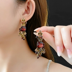 Detail of vintage gold earrings with autumn leaf gems and square red stone on model