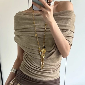 French vintage style long gold shell tassel necklace on a beige off-shoulder pleated top