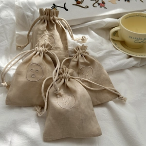 Detail of four linen drawstring pouches with embroidered faces on white fabric