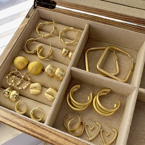 Golden geometric earrings set with hoop and heart designs in a wooden jewelry box