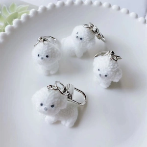Cute white flocked puppy keychains with silver metal clips on a ceramic tray