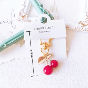 Detail of a shiny cherry keychain with gold leaf and star hook on a thank you card