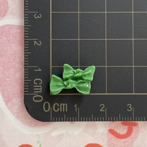 Nahaufnahme kleiner 1,5 cm grüner Harzschleifen auf Schneidematte für DIY-Basteln