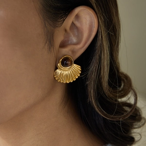 Close-up of a gold fan-shaped earring with dark tiger eye stone worn on model's ear