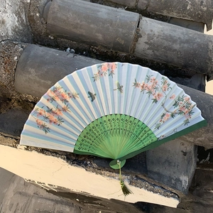 Detail of a Chinese folding fan featuring peach blossoms, birds, and a green silk tassel