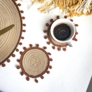 Detail of round woven placemats with brown pom-pom edges and natural texture