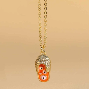 Detailed close-up of golden flip-flop pendant with orange enamel and evil eye charms