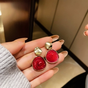 Detailed close-up of red tulip bow earrings with gold frames held in hand for scale
