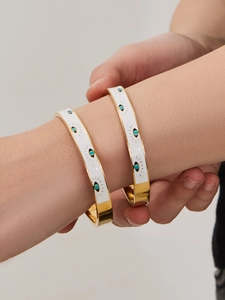 Macro shot of two gold-plated stainless steel evil eye bangles with white enamel inlay