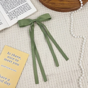 Classic green ribbon bow hair clip in soft satin fabric displayed on waffle texture fabric