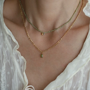 Detail of layered olive green beaded necklace and golden emerald pendant on a model