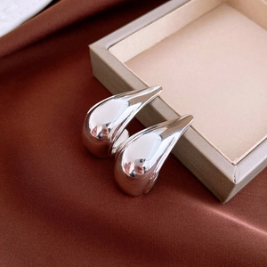 Detail of glossy silver teardrop earrings placed on silk fabric and jewelry box