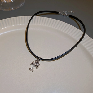 Close-up of black leather choker with silver cross pendant on a white ceramic tray
