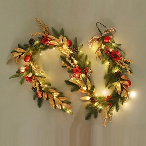 Close-up of Christmas garland with pine needles, red ornaments, gold leaves, and LED lights