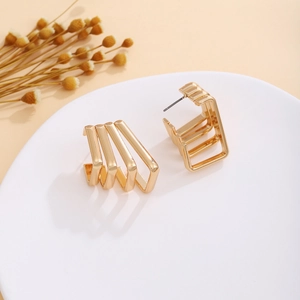 Macro detail of gold geometric layered rectangular earrings on a white minimalist plate