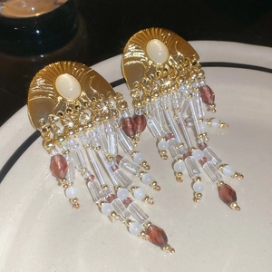 Macro shot of vintage gold tassel earrings with pearl and crystal beads on a ceramic tray