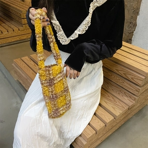 Close-up of fluffy yellow and brown checkerboard plush tote bag held by a model