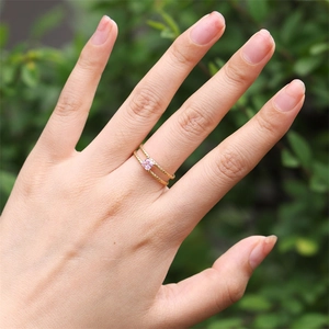 Close-up of a double-layered gold ring with a pink square zircon on a model's finger