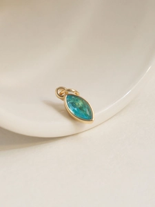 Detail of an 18K gold plated oval pendant with a marquise blue zircon on a ceramic dish