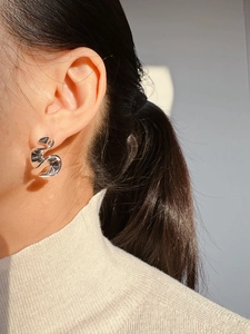 Macro side view of silver irregular fluid metal stud earrings on a female model
