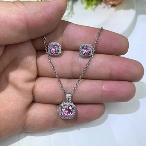 Detail of pink zircon necklace and square stud earrings jewelry set held by hand
