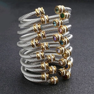 Rainbow gemstone steel cable bracelets with gold accents on a dark textured background