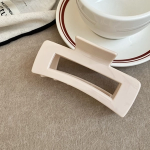 Detail of a minimalist cream rectangular hollow hair claw clip on felt background