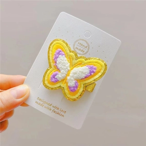 Detail of a handmade plush butterfly hair clip with yellow embroidery and golden glitter edge