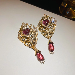 Close-up of vintage gold earrings featuring red heart crystals and white rhinestones